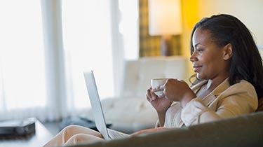 Woman holding coffee cup looking at laptop